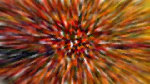 Abstrakte, stark verwischte Aufnahme mit radialen Streifen in Rot, Orange, Grün und Weiß, die von einem dunkleren Zentrum nach außen strahlen.