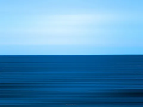 Horizontal verwischte Streifen in Blau: heller Himmel über einer dunkelblauen Wasserfläche, getrennt durch eine klare Horizontlinie.