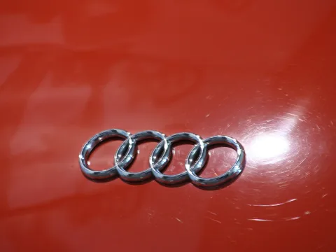 Chromfarbenes Audi-Emblem mit vier ineinandergreifenden Ringen auf roter, glänzender Autolackierung.