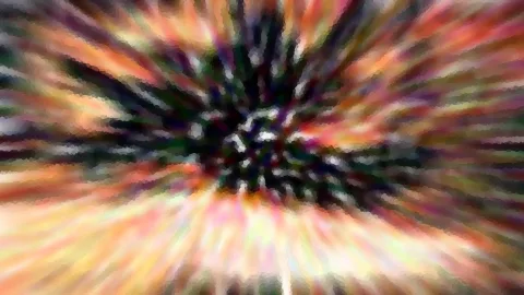 Abstrakte Unschärfe mit radial von einem dunklen Zentrum ausstrahlenden Streifen in Orange, Violett, Grün und Gelb.