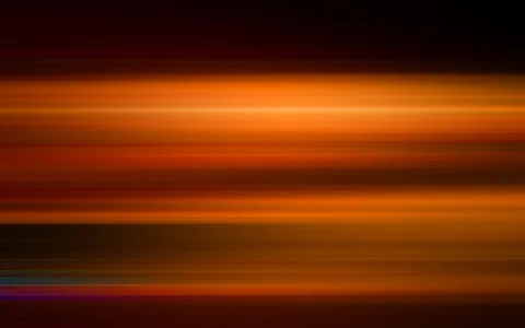 Horizontal verwischte Streifen in Orange, Rot und Dunkelbraun, oben und unten dunkel, unten links kühle blaue und violette Schlieren.