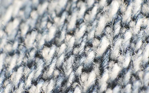 Nahaufnahme eines grau-blauen Stoffs mit diagonaler Köperbindung, an dem einzelne Fasern abstehen.