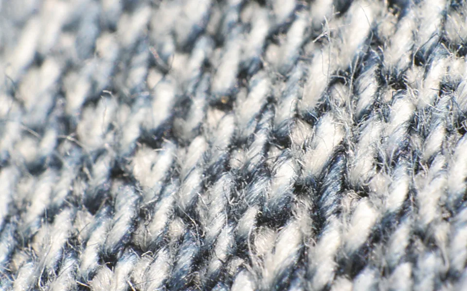 Nahaufnahme eines grau-blauen Stoffs mit diagonaler Köperbindung, an dem einzelne Fasern abstehen.