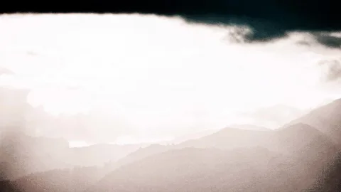 Mehrere hintereinanderliegende Bergkämme im Dunst, darüber eine helle Wolkendecke mit dunklem Streifen am oberen Rand.