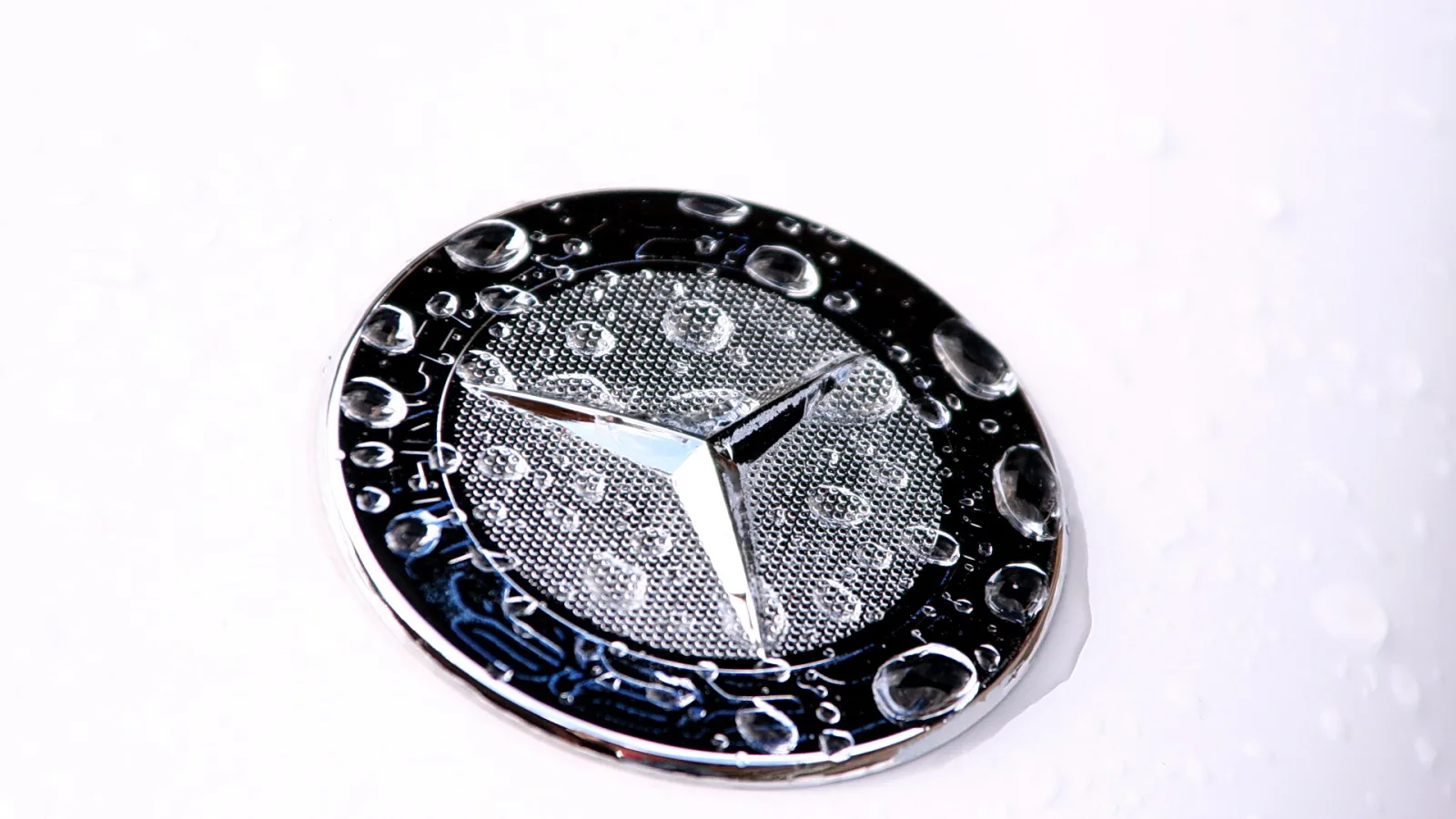 Chromfarbenes Stern-Emblem mit Wassertropfen auf einer weißen Fläche.