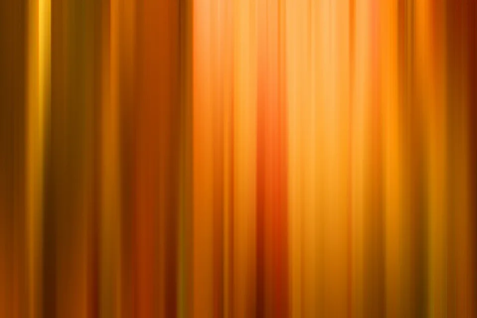 Abstrakte, vertikal verwischte Streifen in Orange, Gelb und Rot, die von dunklen Rändern zu einem hellen Mittelbereich verlaufen.