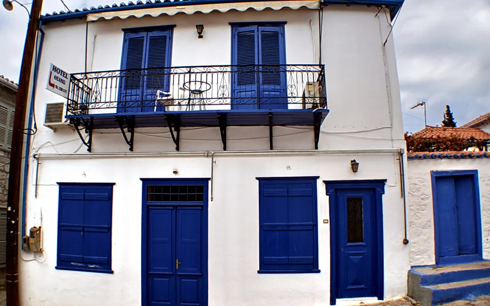 Weiß getünchtes zweistöckiges Haus mit blauen Fensterläden, blauen Türen und einem Balkon mit schmiedeeisernem Geländer.