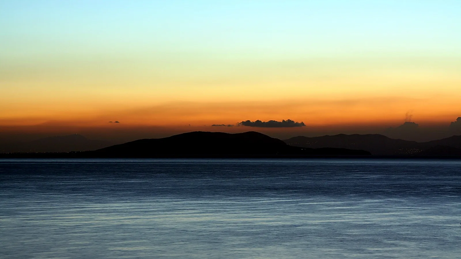 Dunkle Inselsilhouetten vor einem orange-blau verlaufenden Abendhimmel über ruhigem Meer.