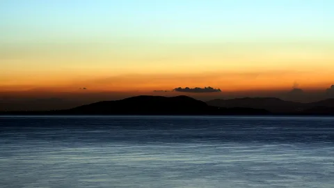Dunkle Inselsilhouetten vor einem orange-blau verlaufenden Abendhimmel über ruhigem Meer.