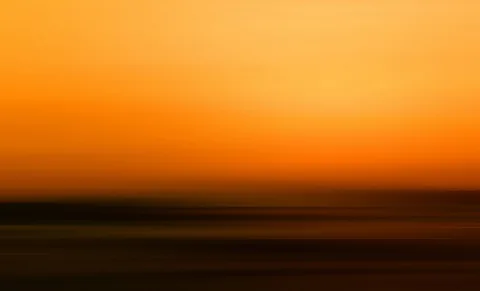 Verwischte horizontale Streifen in Orange und Gelb, oben heller Himmel, unten dunkle Schichten am Horizont.
