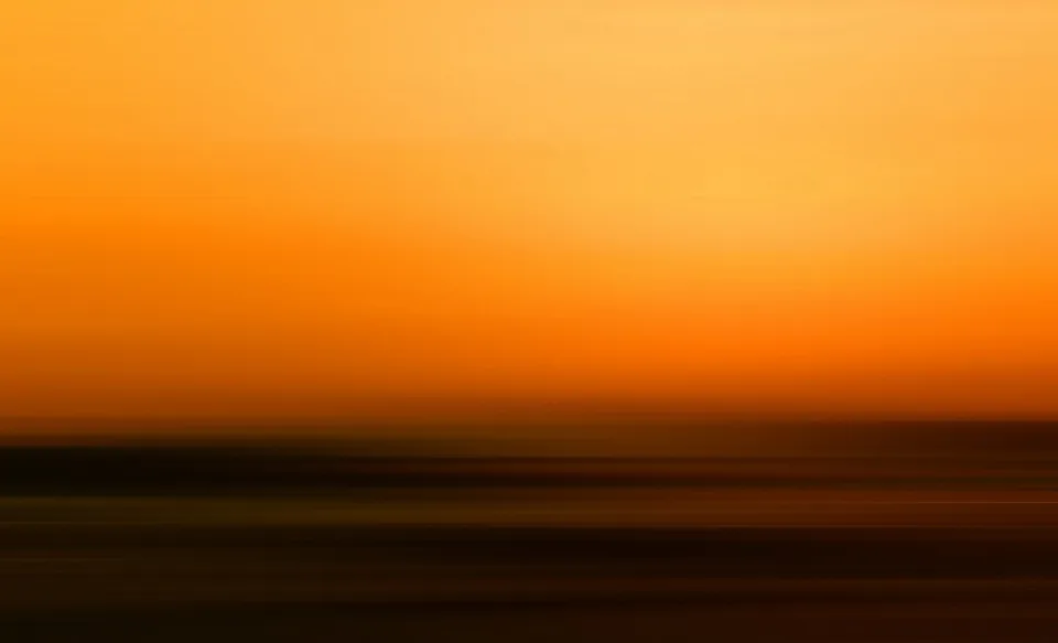 Verwischte horizontale Streifen in Orange und Gelb, oben heller Himmel, unten dunkle Schichten am Horizont.