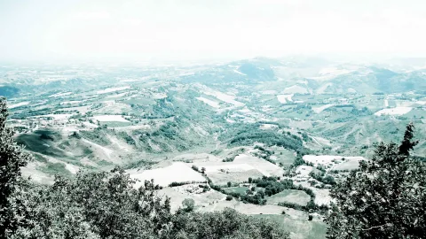 Blick von einer Anhöhe über weite, hügelige Landschaft mit Feldern, kleinen Ortschaften und Baumgruppen im Vordergrund, überzogen von hellem Dunst.