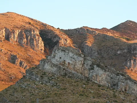 Steil aufragende, geschichtete Kalkfelsen über trockenem, goldbraunem Gras im warmen Abendlicht vor klarem Himmel.