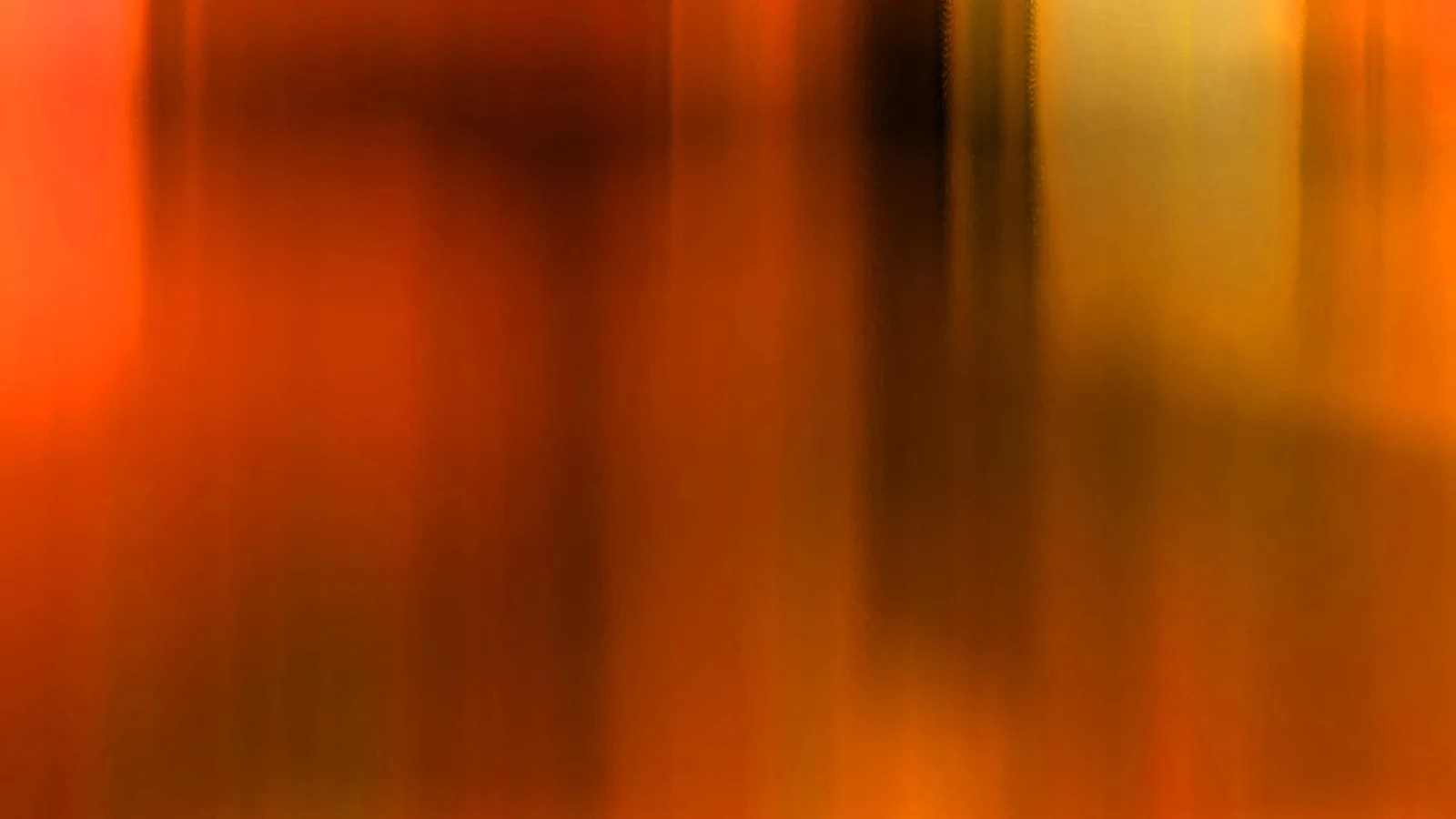 Abstrakte, vertikal verwischte Streifen in Orange, Rot und Dunkelbraun, rechts ein helles Gelb.