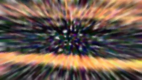 Abstrakte Komposition aus bunten, radial von einem dunklen Zentrum nach außen laufenden Farbstreifen in Orange, Lila und Grün, mosaikartig verpixelt.
