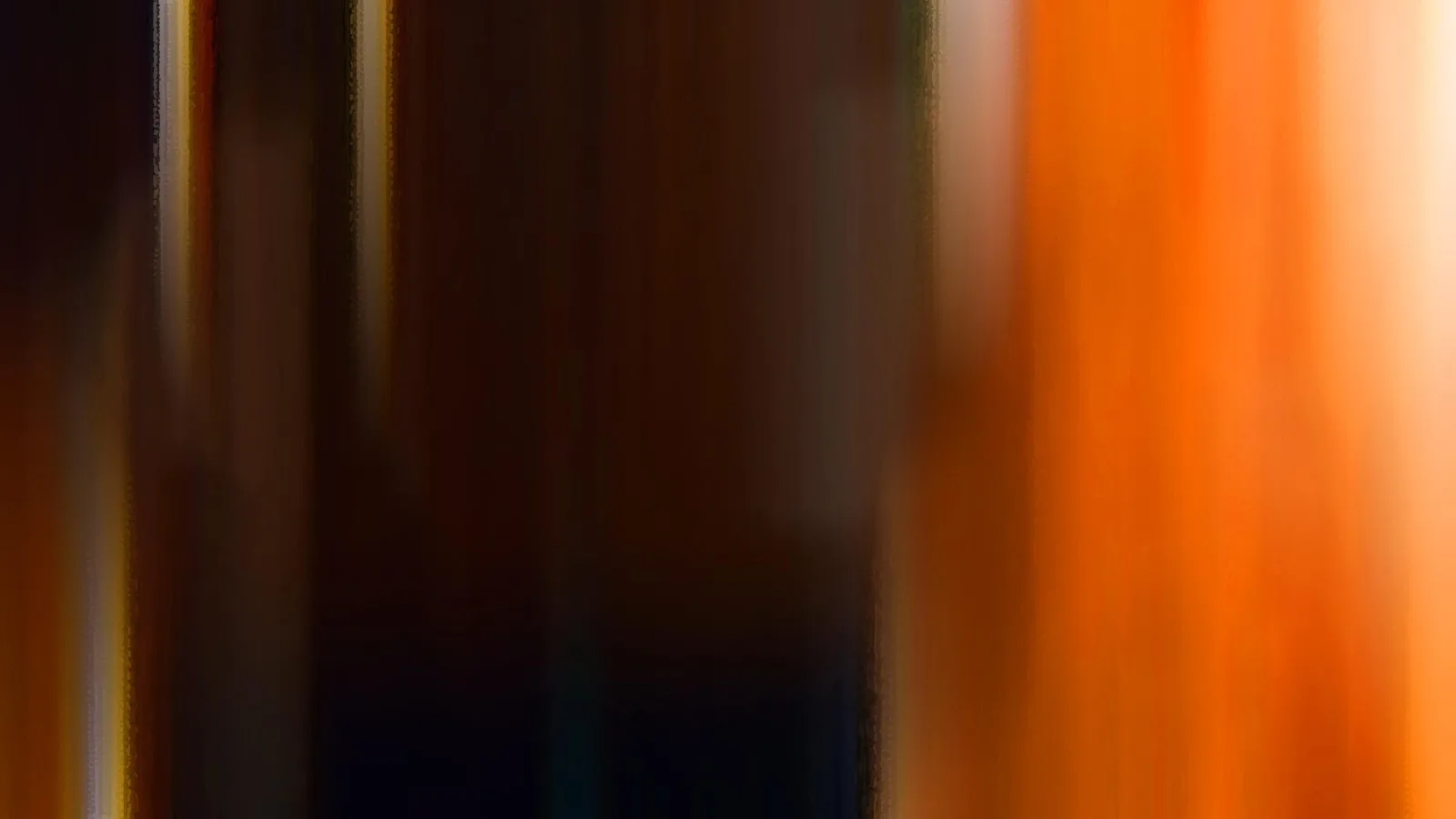 Abstrakte, vertikal verwischte Aufnahme mit dunkler Mitte und hellen Streifen links sowie orangefarbenem Licht rechts.