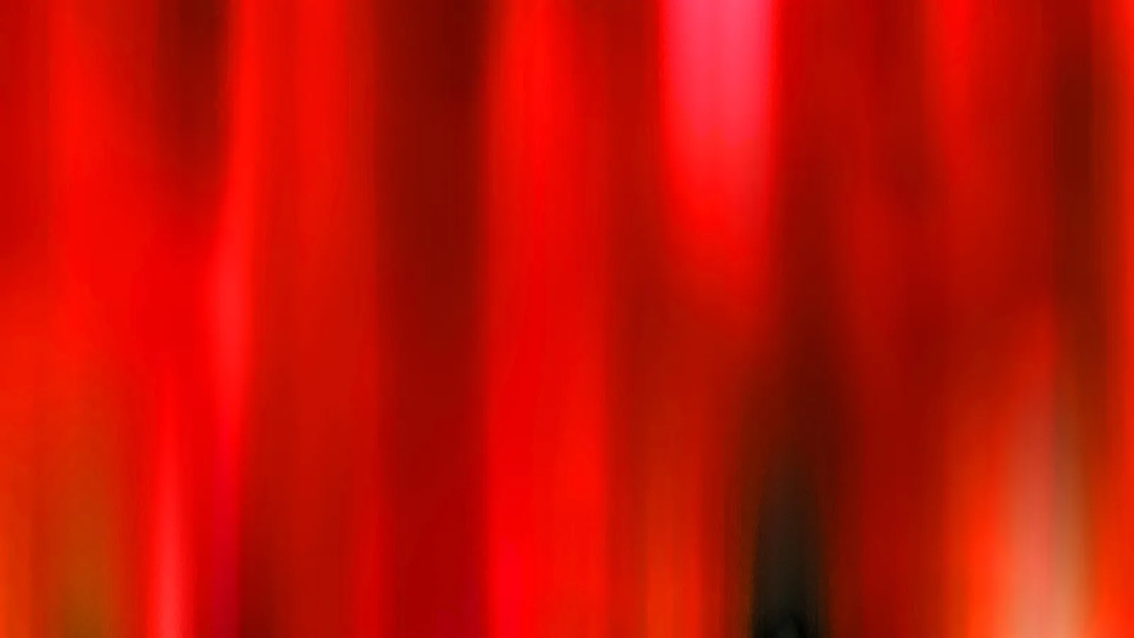 Abstrakte, vertikal verwischte Streifen in Rot und Rosa mit einem dunklen Fleck unten rechts.