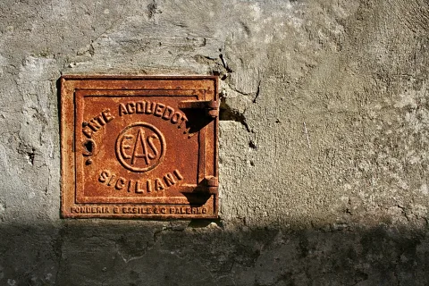 Quadratische rostige Gusseisenklappe mit erhabener Schrift in einer verwitterten grauen Putzwand