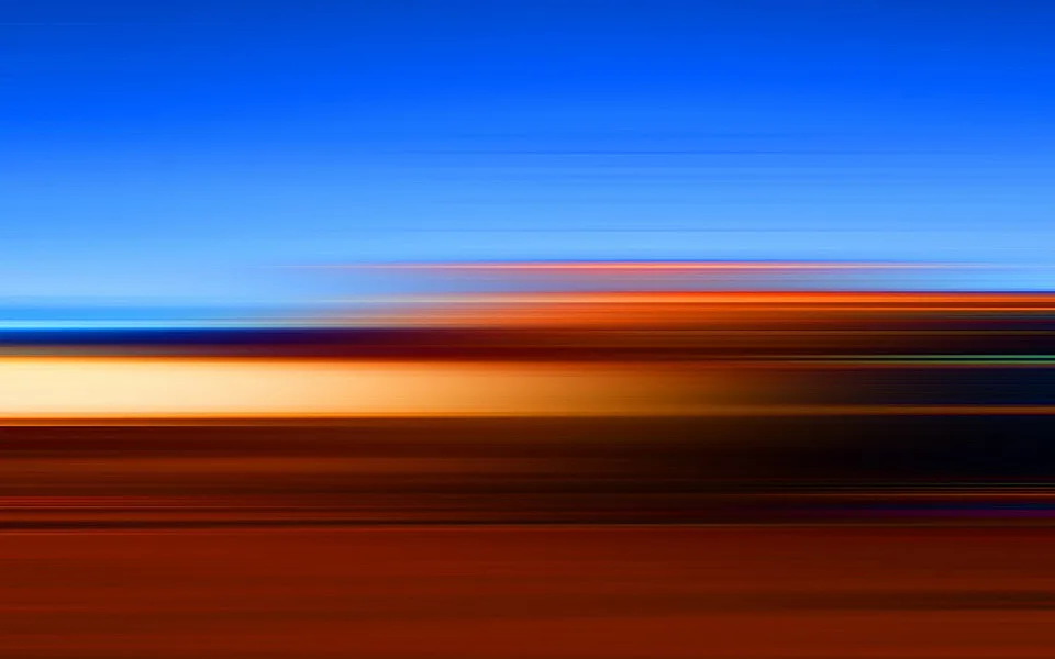 Abstrakte Komposition aus horizontalen Streifen: oben tiefblauer Himmel, darunter orange, cremefarbene und dunkelbraune Bänder, die wie Lichtspuren verwischen.