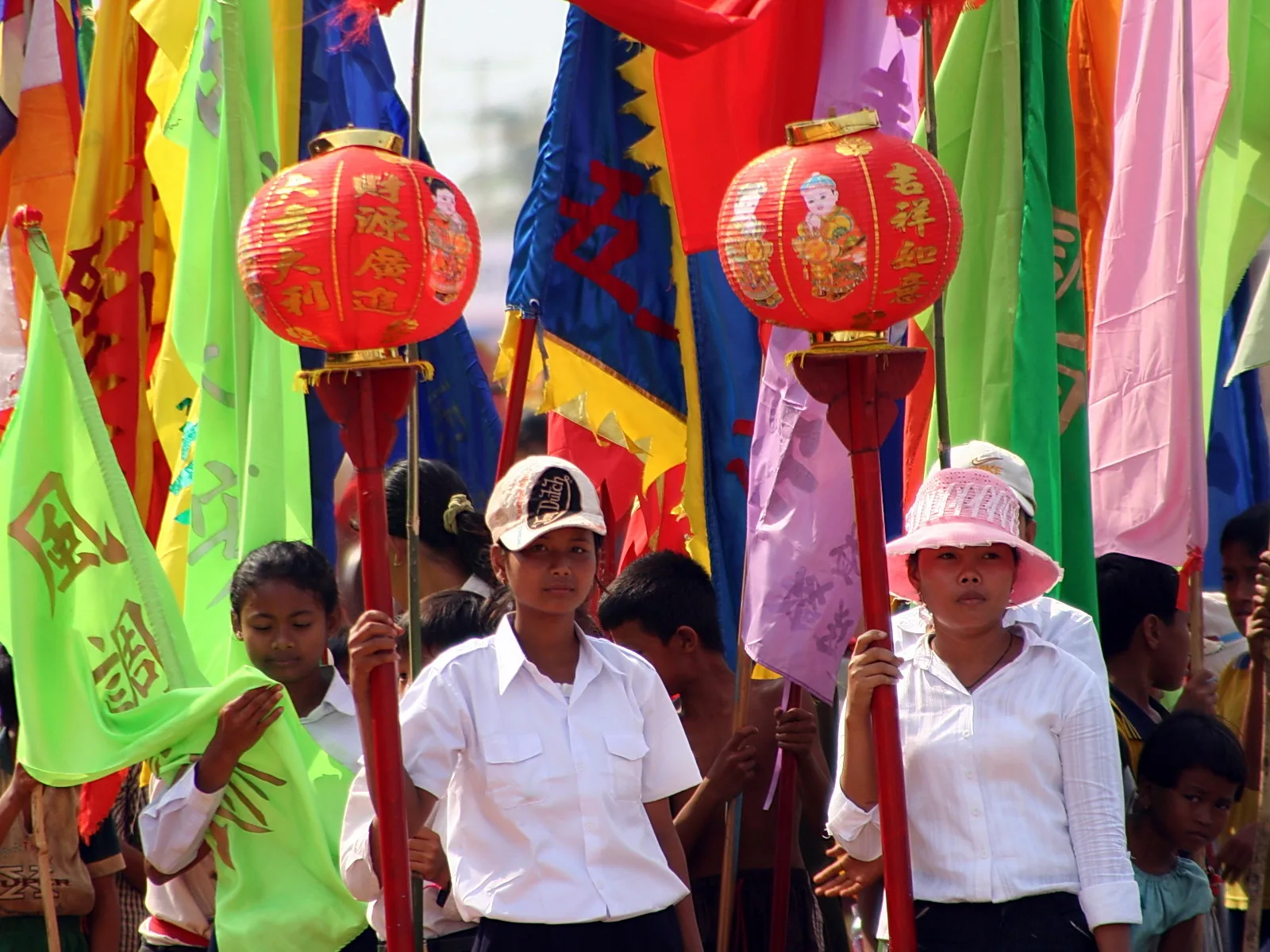 Festumzug mit Teilnehmern in weißen Hemden, die lange bunte Fahnen und rote Lampions mit chinesischen Schriftzeichen tragen.