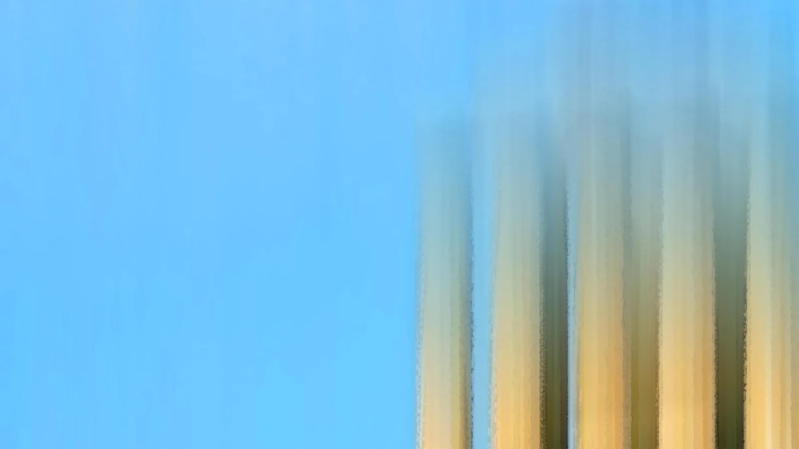 Rechts verwischte, vertikale Streifen in Gelb, Beige und Dunkelgrün vor einem klaren blauen Himmel, links nur einfarbige Fläche.