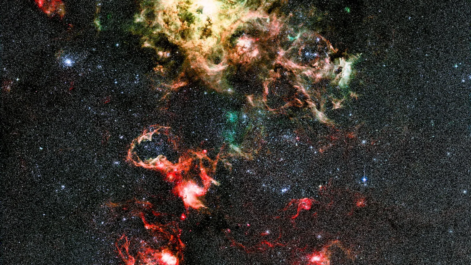 Rot, gelb und grün leuchtende Gasnebel vor einem dichten Sternenfeld im Weltraum.