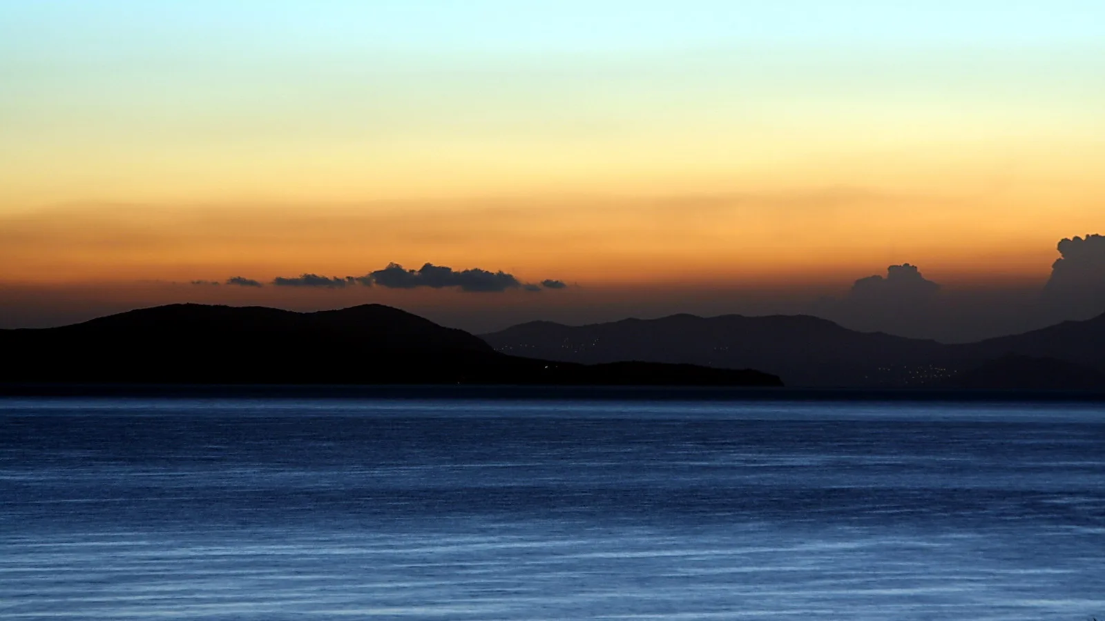 Dunkle Inselsilhouetten vor einem Meer unter einem Himmel mit orangefarbenem Horizont und blauem Abendhimmel