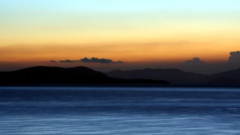 Dunkle Inselsilhouetten vor einem Meer unter einem Himmel mit orangefarbenem Horizont und blauem Abendhimmel