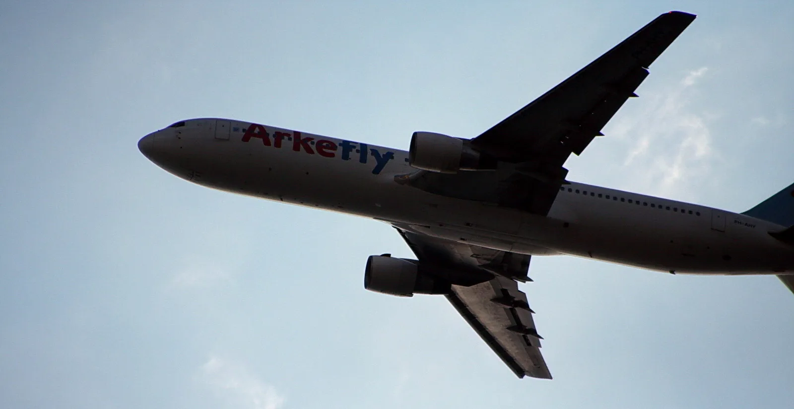 Ein weißes Passagierflugzeug mit roter und blauer Aufschrift Arkefly steigt schräg von unten nach oben vor einem hellblauen Himmel auf, Triebwerke und Tragflächen sind gut zu erkennen.