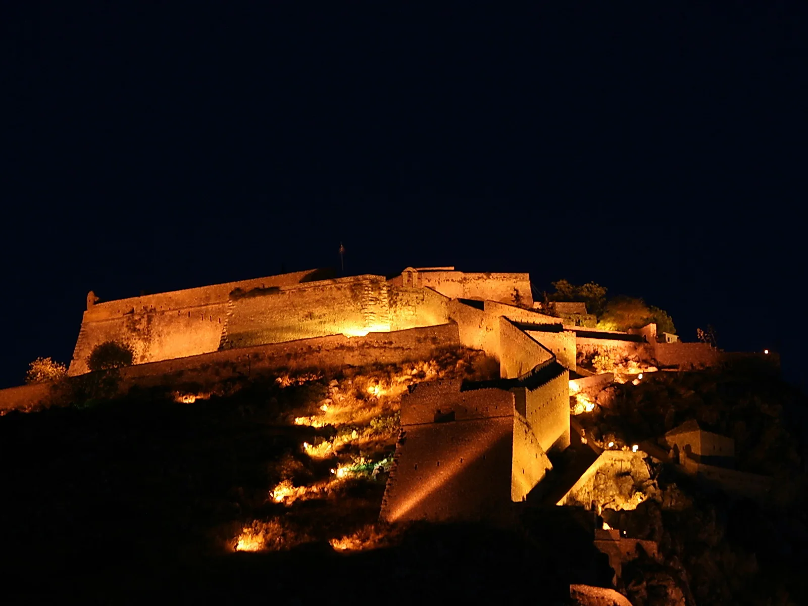 Beleuchtete Burgmauern und Bastionen auf einem Hügel vor dunklem Nachthimmel