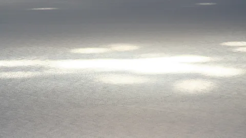 Graue Meeresoberfläche mit mehreren hellen Sonnenreflexen, die sich über das Wasser verteilen.