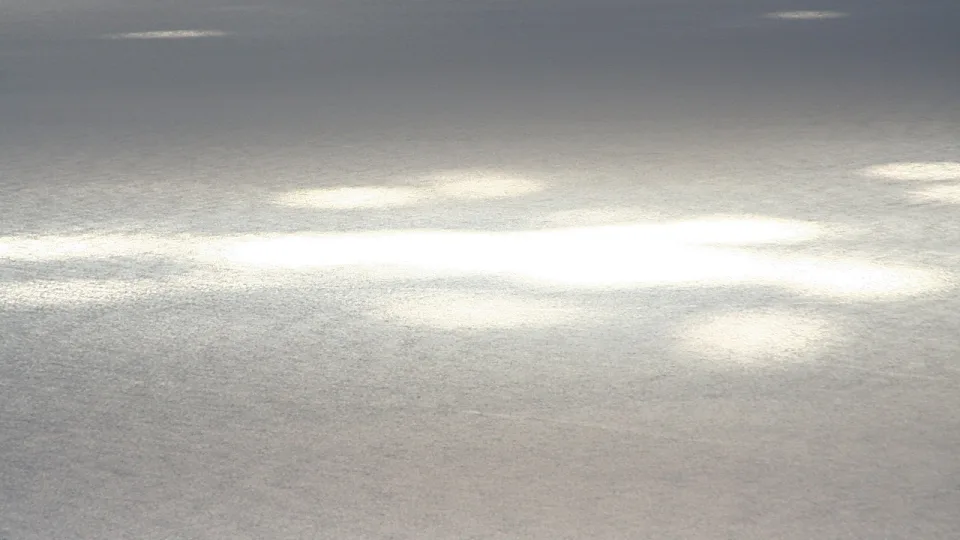 Graue Meeresoberfläche mit mehreren hellen Sonnenreflexen, die sich über das Wasser verteilen.