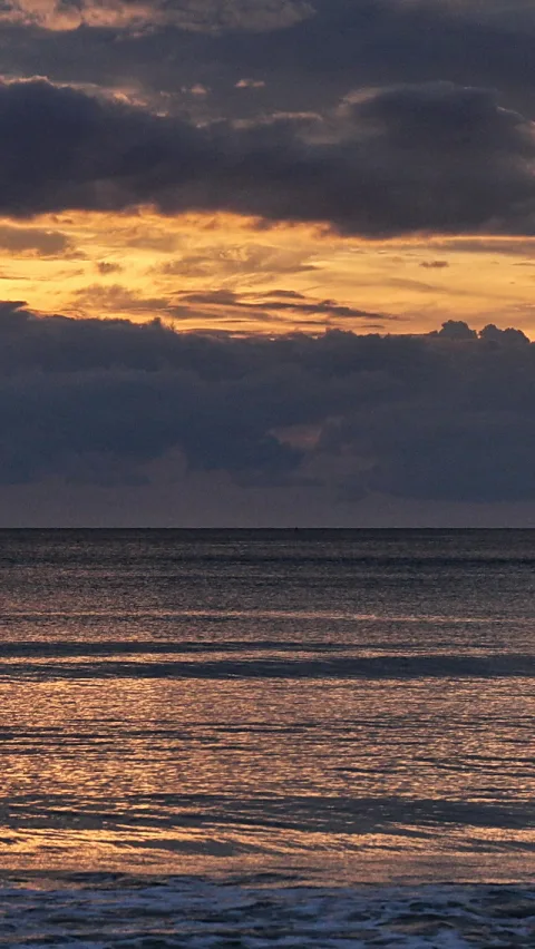 Dunkle Wolkenbänke über einem ruhigen Meer, am Horizont glüht der Sonnenuntergang golden.