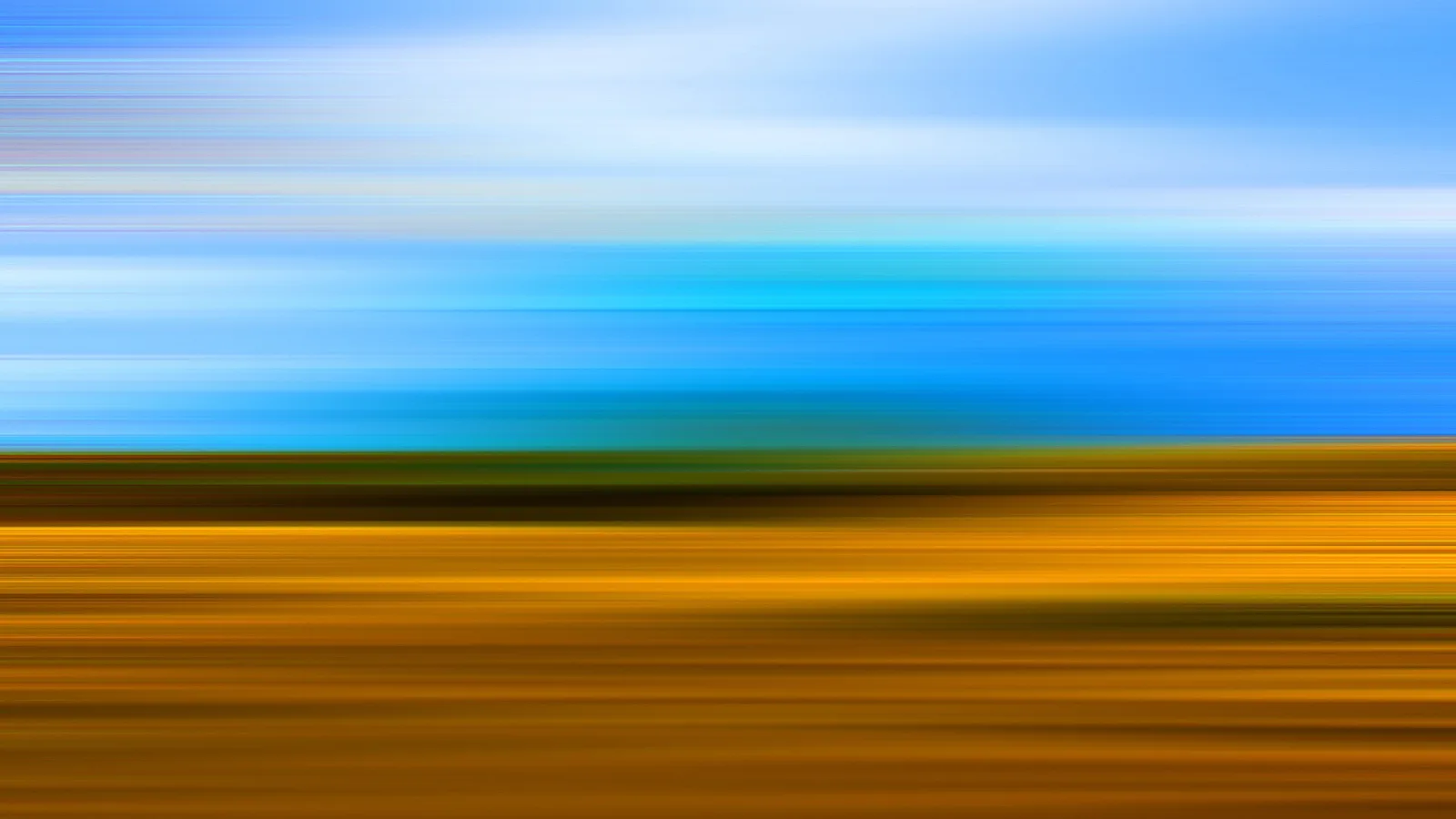 Horizontal verwischte Aufnahme: oben blauer Himmel mit hellen Schlieren, unten ein goldgelbes Feld mit einem grünlichen Horizontstreifen.