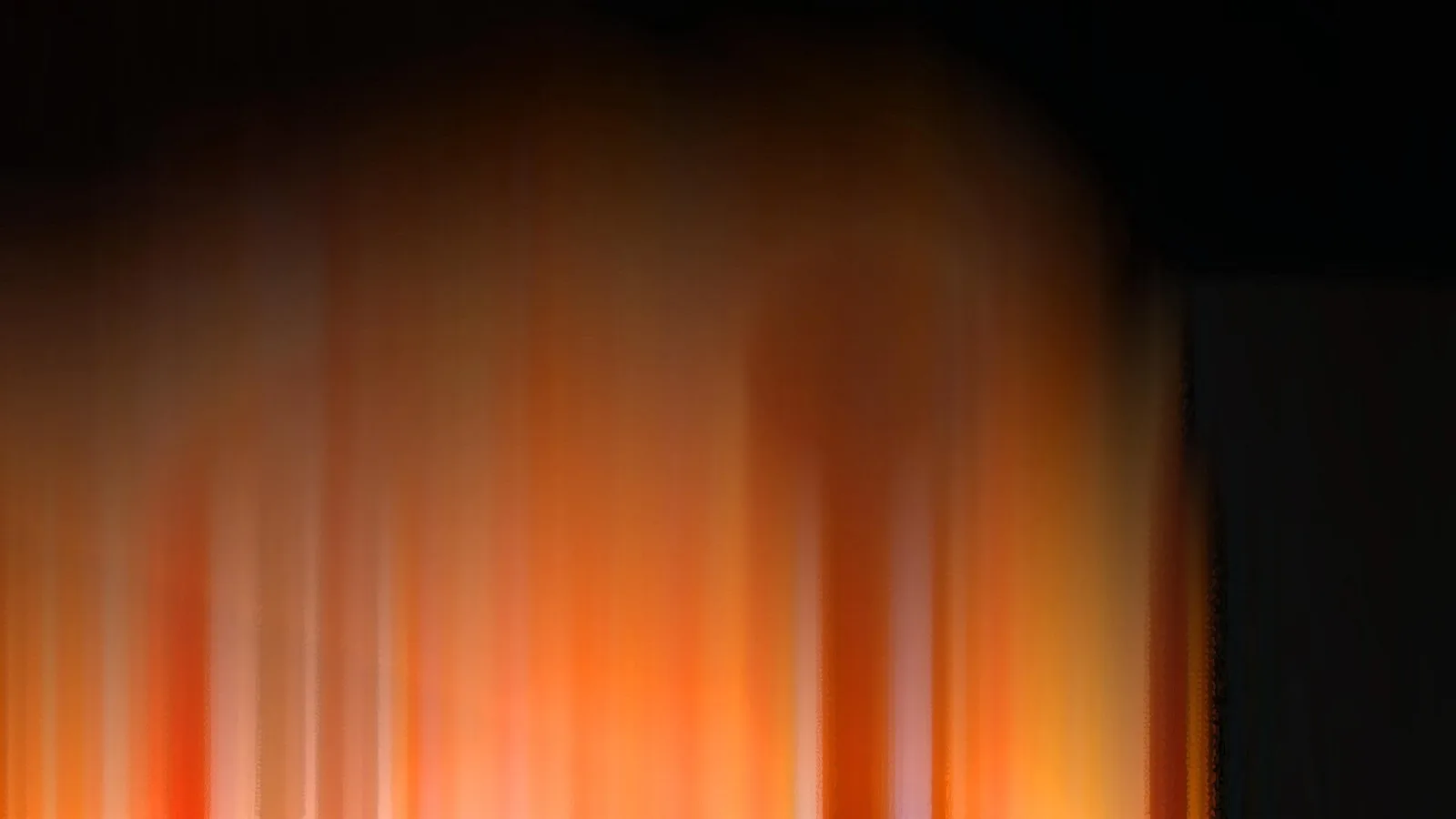 Vertikal verwischte orangefarbene und gelbe Lichtstreifen, die von unten nach oben in eine schwarze Fläche übergehen, rechts ein dunkler Block.