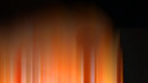Vertikal verwischte orangefarbene und gelbe Lichtstreifen, die von unten nach oben in eine schwarze Fläche übergehen, rechts ein dunkler Block.