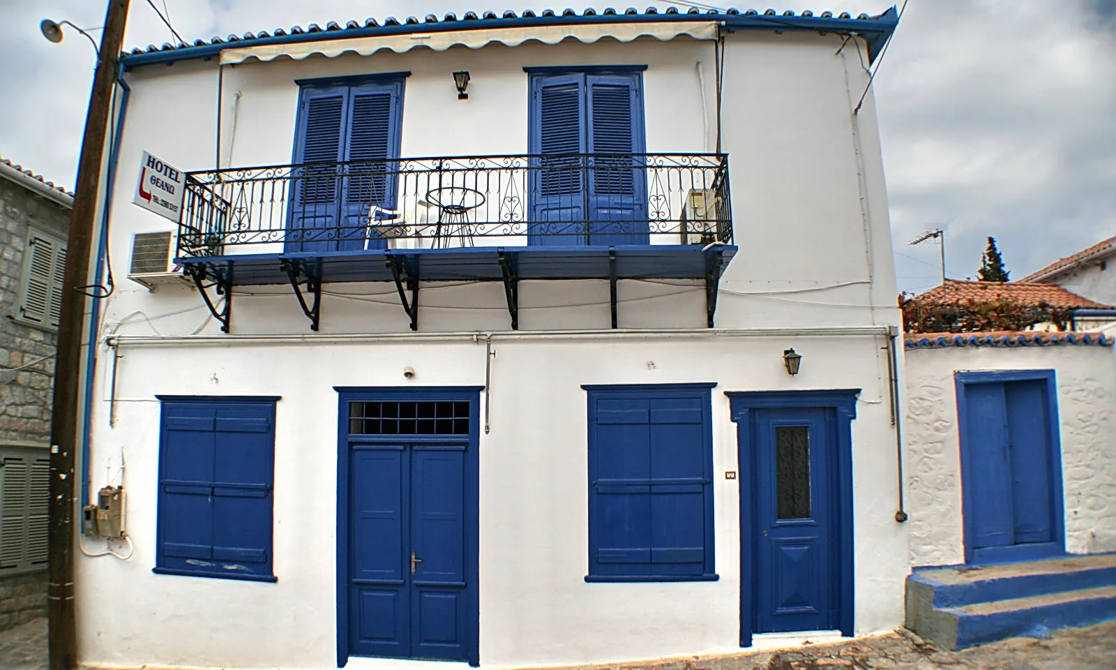 Zweistöckiges, weiß getünchtes Haus mit blauen Fensterläden, blauen Türen und einem schmiedeeisernen Balkon, davor eine Treppe mit blauen Stufen.