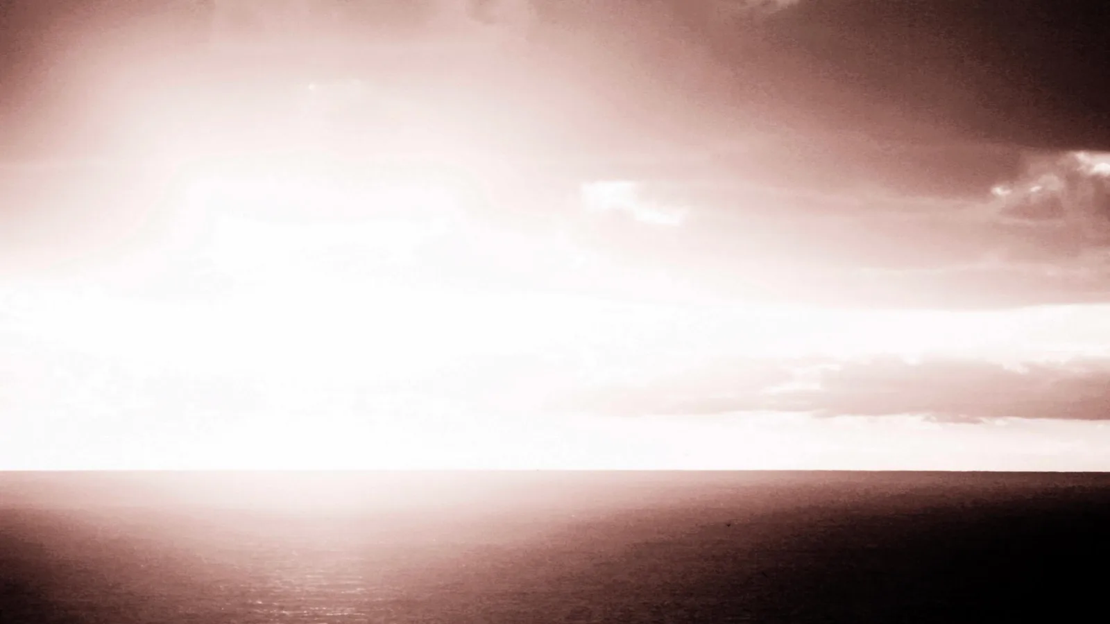 Helles Sonnenlicht hinter Wolken über einer weiten, dunklen Meeresfläche, der Horizont verläuft waagerecht durch die Bildmitte, in warmen Sepiatönen.