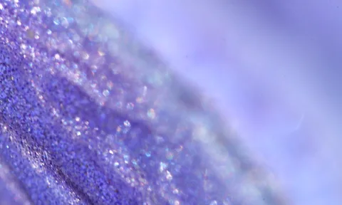 Nahaufnahme einer violetten, glitzernden Oberfläche, die diagonal nach rechts in glatte, helle Lavendelfläche übergeht.