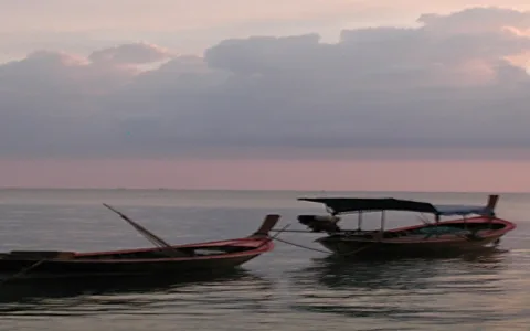 Zwei Longtailboote mit überdachtem Heck liegen auf ruhigem Meer, im Hintergrund rosa gefärbter Abendhimmel mit dunklen Wolken.