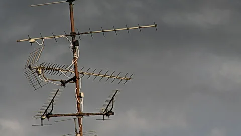 Mehrere alte Fernsehantennen auf einem Metallmast vor einem dunkel bewölkten Himmel.