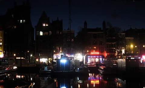 Nächtliche Kanalansicht in Amsterdam mit beleuchteten Giebelhäusern, Booten und Spiegelungen im Wasser.