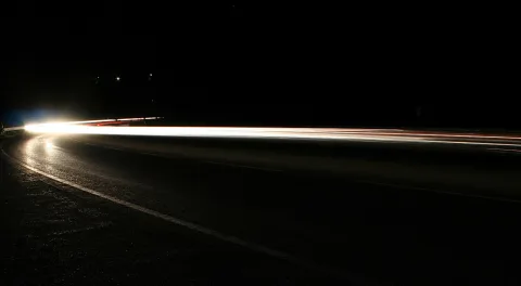 Lange Belichtung einer leeren Straße bei Nacht: Scheinwerferlicht zieht als helle Streifen nach links, der Rest ist schwarz.