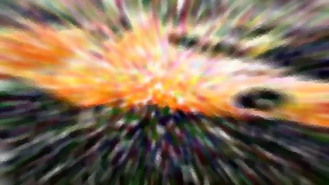 Abstrakte Aufnahme mit radialer Bewegungsunschärfe: orange, gelbe und grüne Farbstrahlen laufen von einem hellen Zentrum nach außen, dunkle Ränder und ein dunkler Fleck rechts.