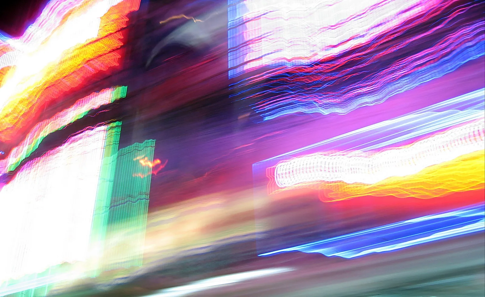 Verwischte Lichtstreifen in Rot, Violett, Blau und Grün vor dunklem Hintergrund, vermutlich Leuchtreklame einer Stadt bei Nacht.
