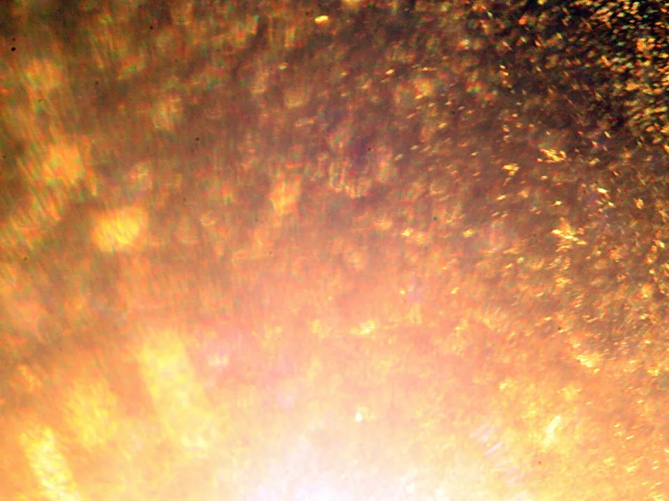 Nahaufnahme einer glitzernden, goldorangefarbenen Oberfläche mit einem hellen Lichtschein im unteren Bereich.