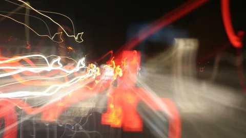 Verwischte Lichtstreifen in Rot, Weiß und Orange vor dunklem Hintergrund, wie bei einer Kamerabewegung in der Nacht aufgenommen.