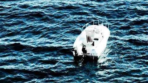 Ein kleines weißes Motorboot mit Reling und Außenbordmotor fährt von oben gesehen auf bewegtem, dunkelblauem Meer.