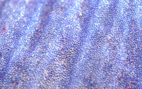 Makroaufnahme einer blau-violetten Oberfläche mit dicht stehenden kleinen Noppen und sanften Falten, die glitzernd das Licht reflektieren.