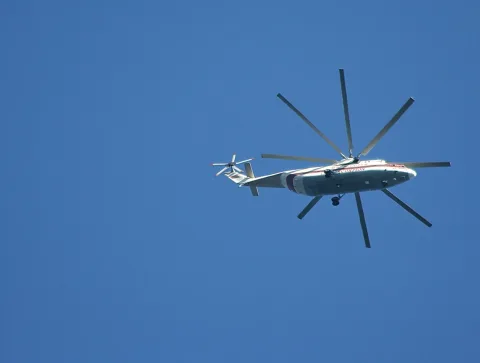 Ein weiß-roter Hubschrauber mit großem Mehrblattrotor fliegt von rechts nach links durch einen wolkenlos blauen Himmel.